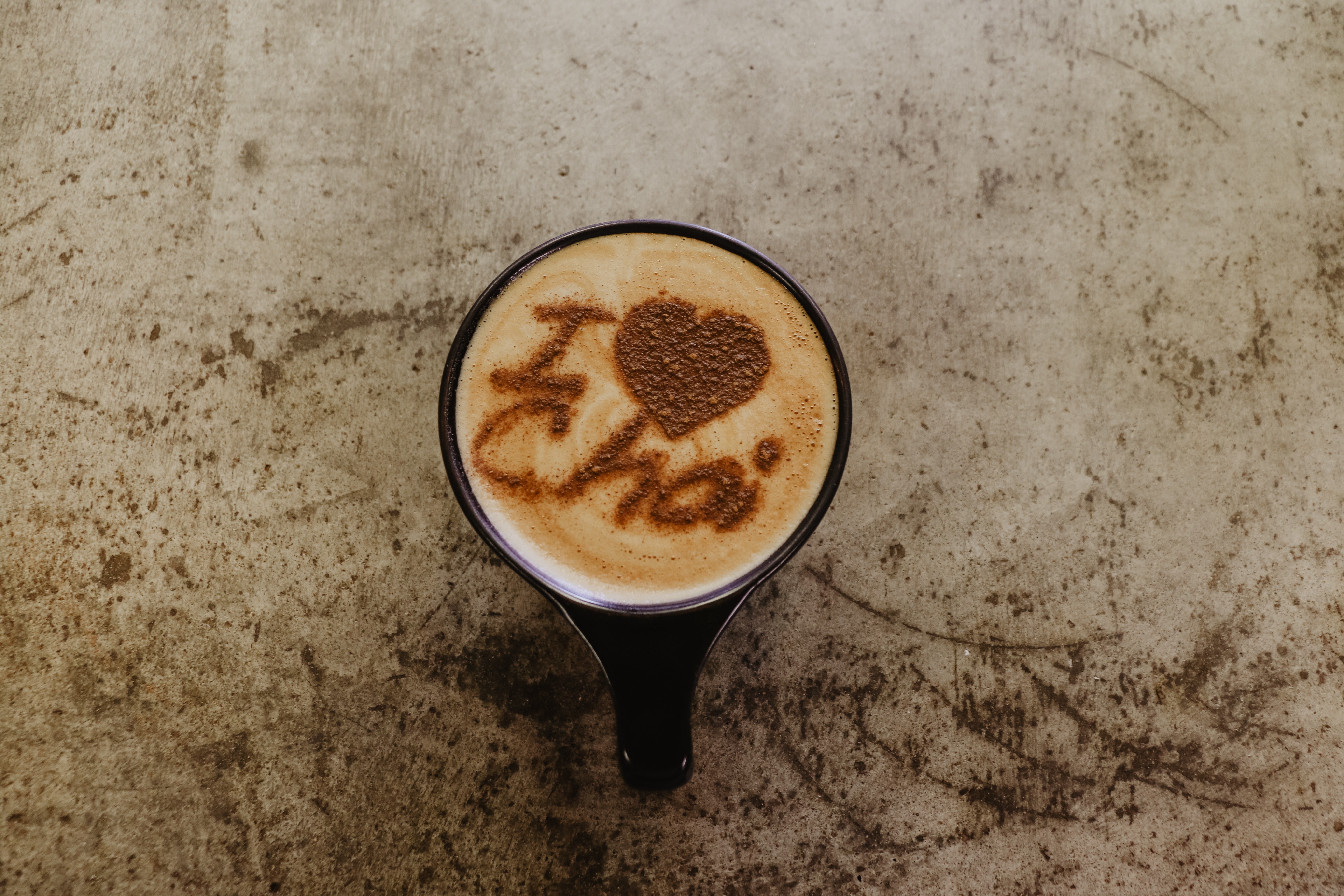 Steaming cup of chai tea with cinnamon stick arranged in the shape of 'I Love Chai' on a marble surface